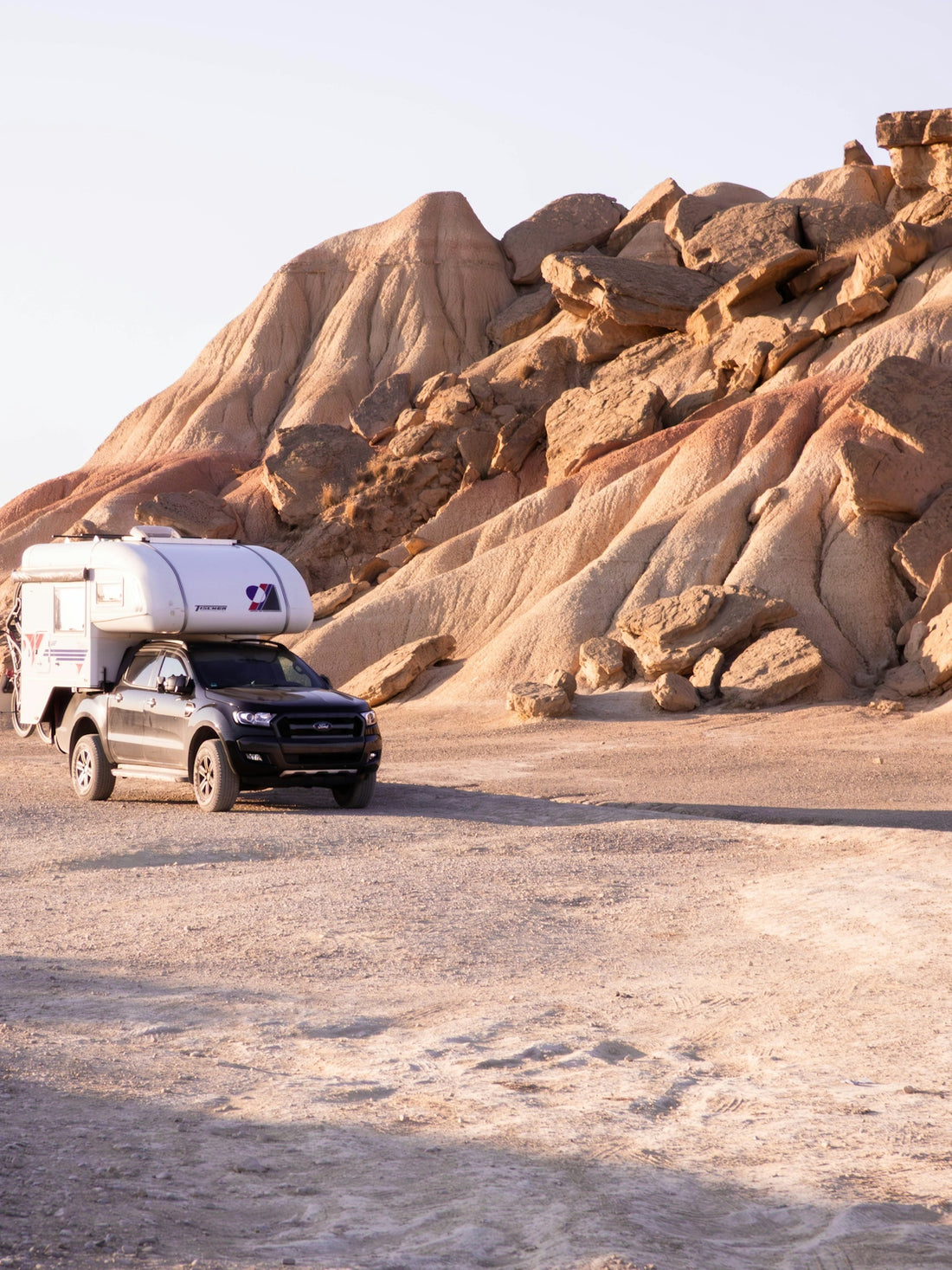 Truck with camper drives through desert landscape.