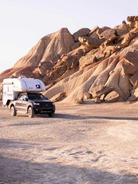 Truck with camper drives through desert landscape.