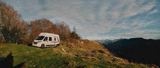 Camper van parked on grassy hillside with mountains beyond.