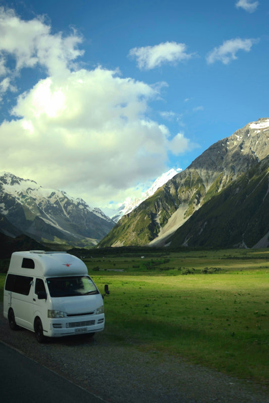 White camper van parked in a green valley with mountains.