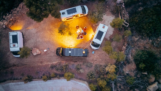 Five camper vans gathered around a campfire at dusk.
