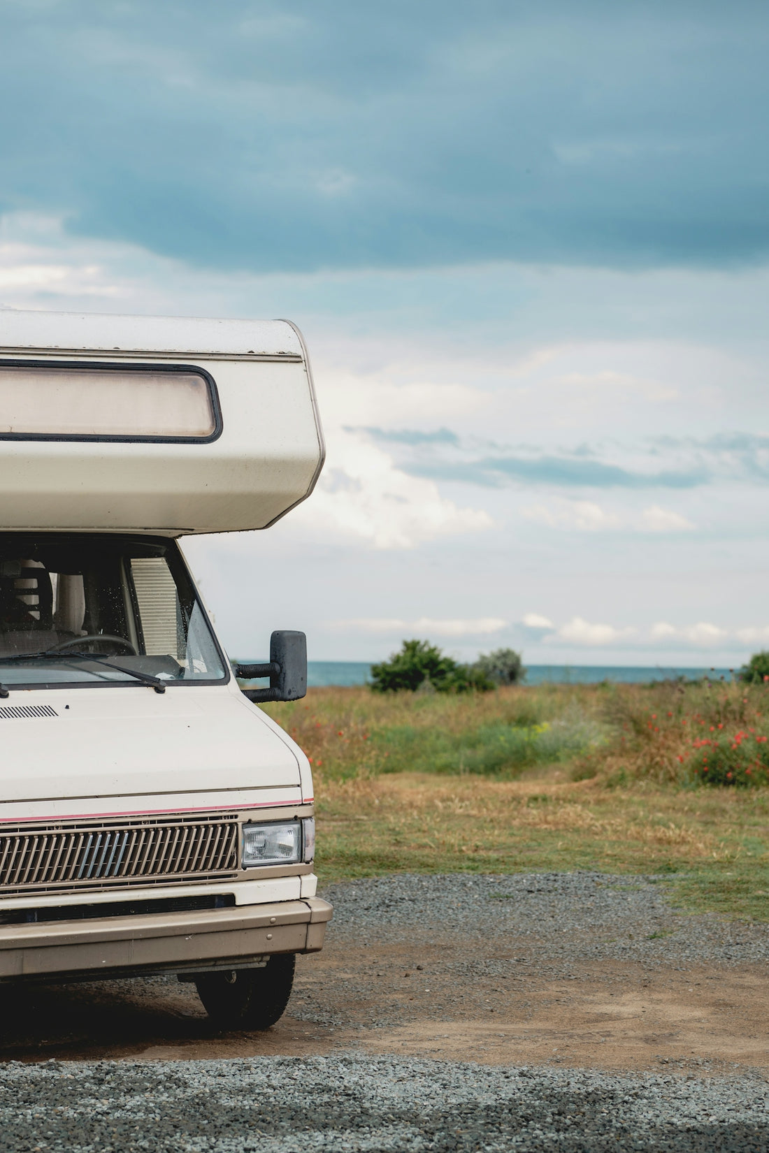 White camper van parked by the ocean under cloudy sky.