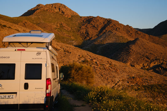 Camper van on dirt road with mountains at sunset.