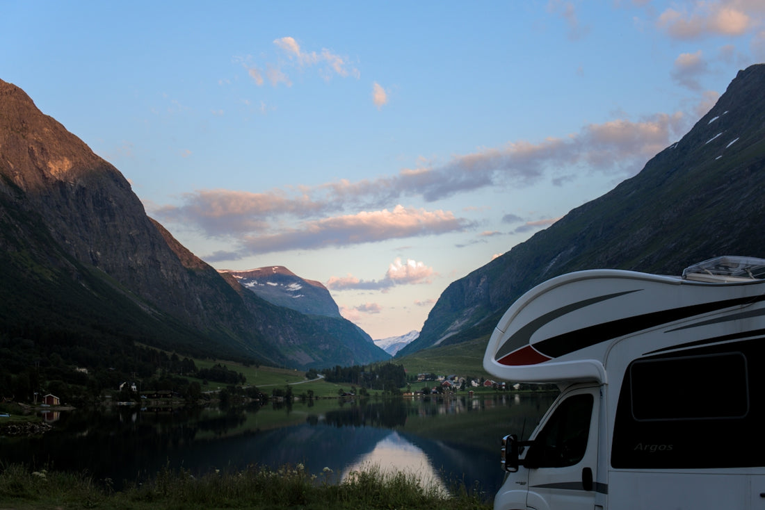 Camper van by a serene lake with mountains at dusk.