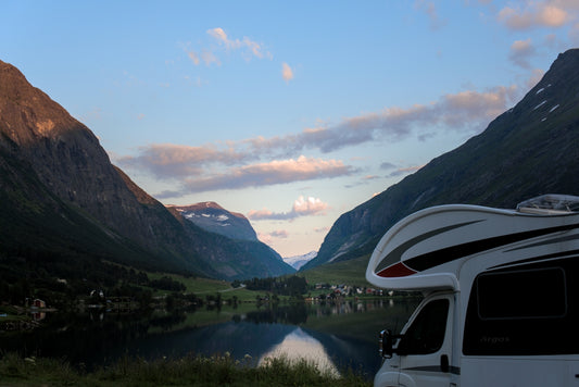 Camper van by a serene lake with mountains at dusk.