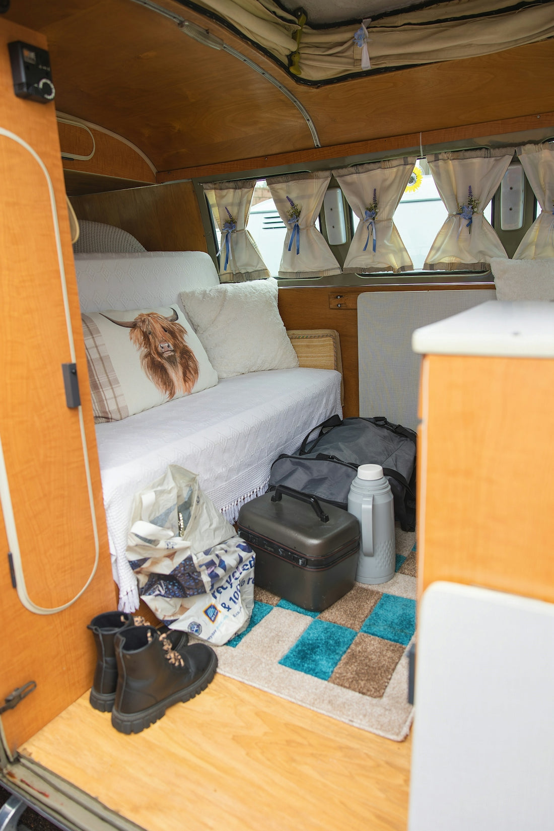 Camper van interior with bedding, bags, boots, and cooler