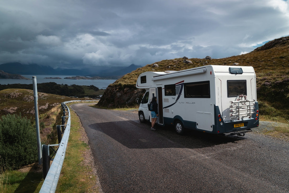 A person entering a motorhome parked on a narrow road beside a coastal landscape