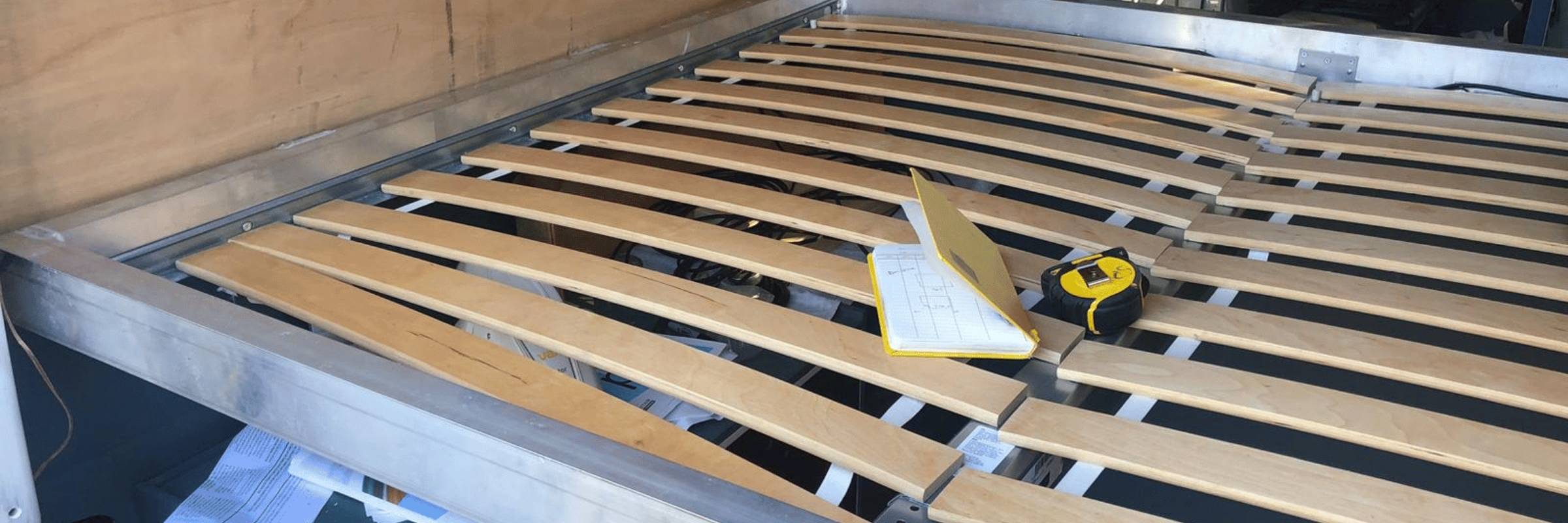 Wooden slats on a metal frame with a measuring tape, in a custom build campervan